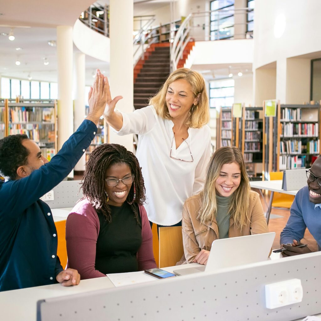 Cheerful diverse group of students collaborating in a library, celebrating with a high five.